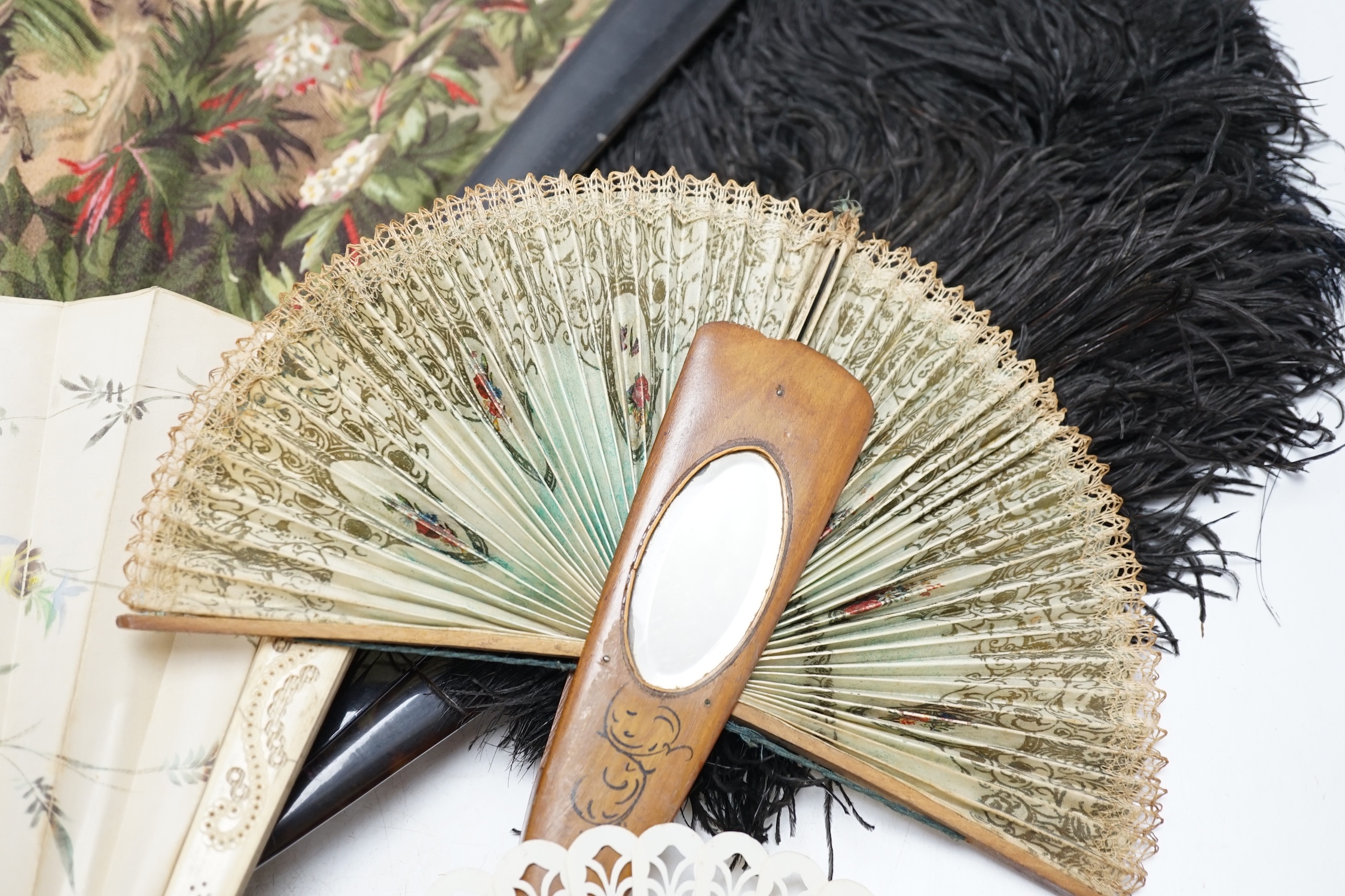 A black ostrich feather and tortoiseshell fan and four others including a carved bone and floral painted silk example. Condition - poor to fair
